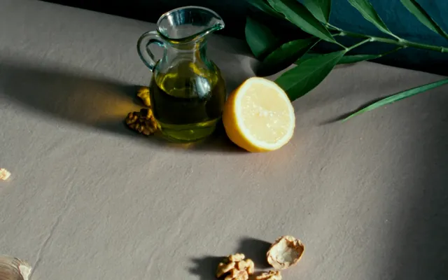 Olio d'oliva, noci, foglie verdi e mezzo limone su un piano di lino